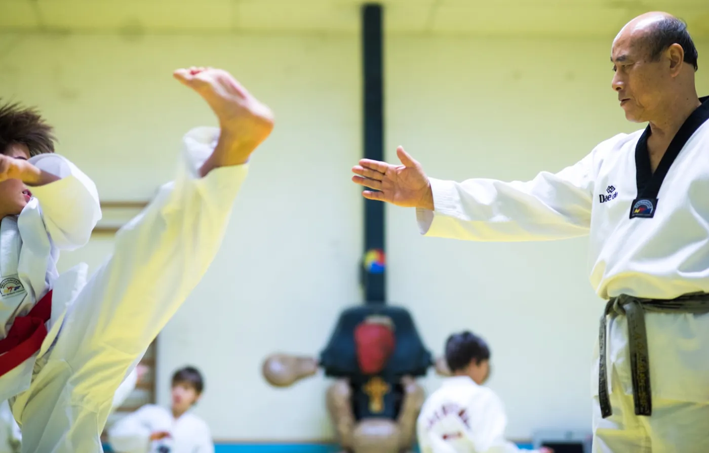 Maître LEE Yong-Seon guidant le coup de pied d’un élève au Taekwondo Mudo Club